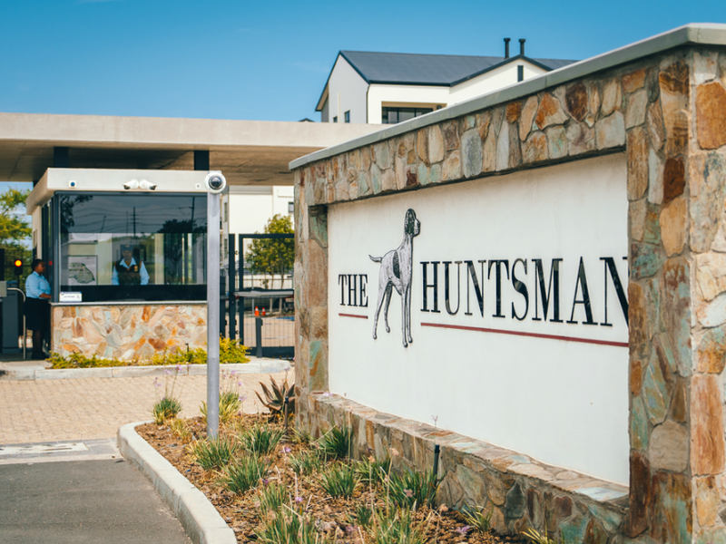 The entrance to The Huntsman estate, featuring a modern security gatehouse, stone-clad signage, and controlled access point.