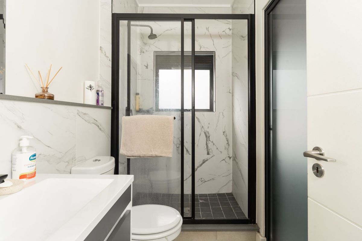 Modern bathroom featuring a walk-in shower with black frame, marble-look wall tiles, vanity unit, and a sleek frosted glass door.