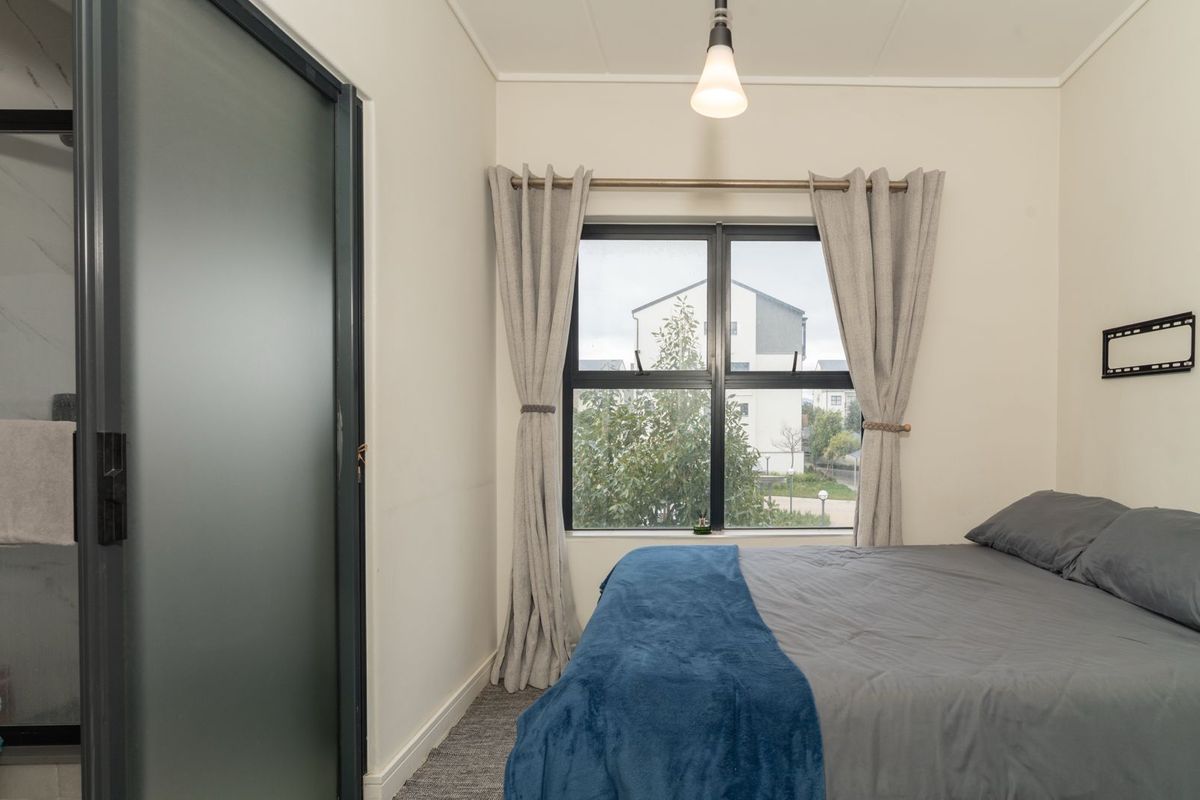A well-maintained bedroom featuring carpeted flooring, a frosted glass door, and an aluminium-framed window with natural light.