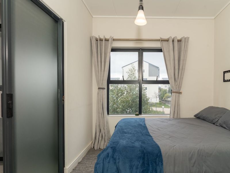 A well-maintained bedroom featuring carpeted flooring, a frosted glass door, and an aluminium-framed window with natural light.