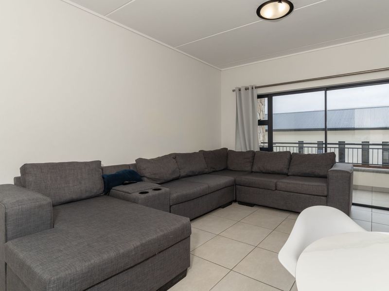 A bright living room featuring neutral tiled flooring and a large sliding glass door providing access to an outdoor balcony area.