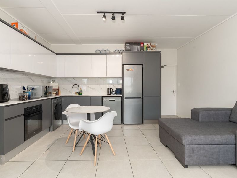 Modern open-plan kitchen and living area featuring sleek two-tone cabinetry, marble-look splashback, integrated appliances, and neutral tiled flooring.