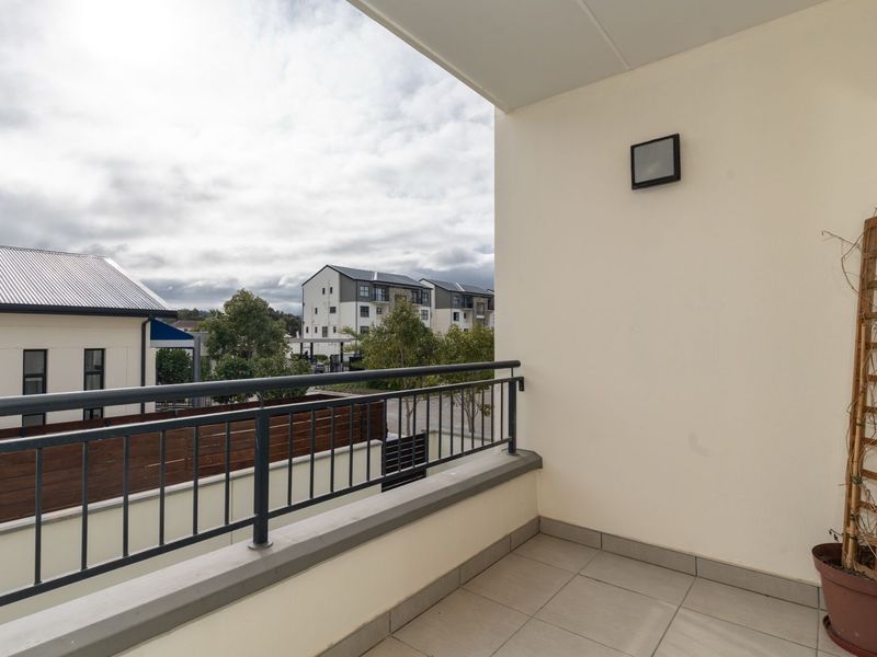 A clean, covered balcony featuring tiled flooring, a metal balustrade, and an exterior wall light, offering a view of the surrounding residential complex.