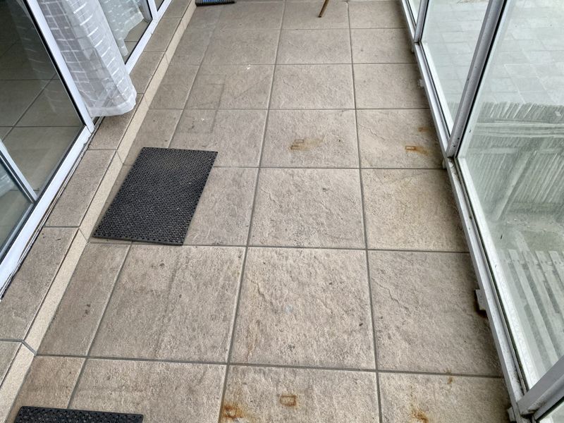 A balcony area featuring tiled flooring and sliding glass doors, showing some surface staining on the tiles.