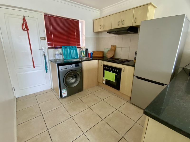 A functional kitchen featuring light wood cabinetry, granite countertops, a built-in oven with hob, and tiled flooring.