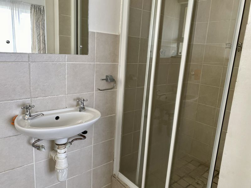 A functional bathroom featuring a wall-mounted basin, tiled walls, and a glass-enclosed shower unit.
