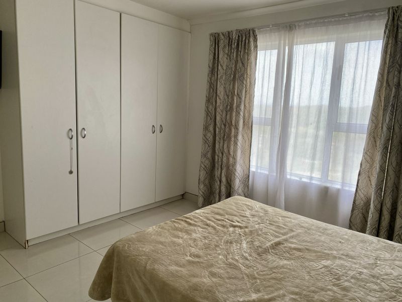 A bright bedroom featuring neutral tiled flooring and ample built-in cupboard storage with natural light from a large window.