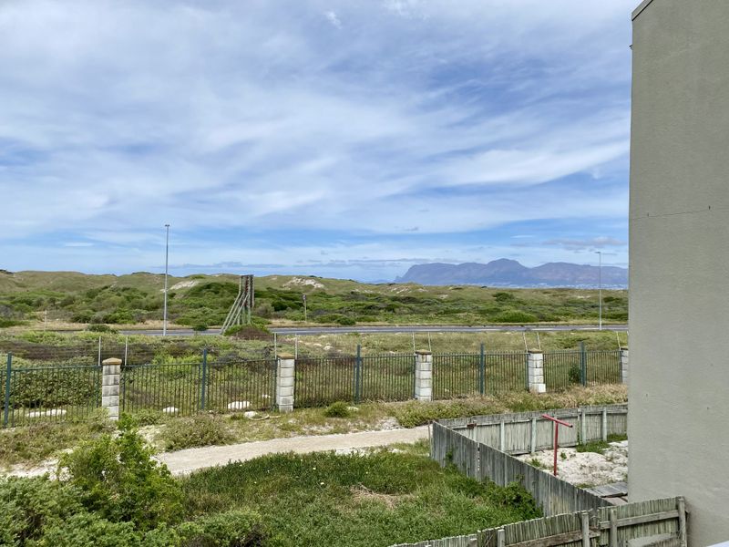 An elevated view overlooking a coastal landscape with natural dunes, mountain vistas, and perimeter security fencing.