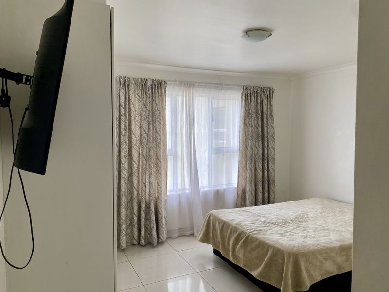 A simple bedroom featuring tiled flooring, a central ceiling light, and a window with curtains.