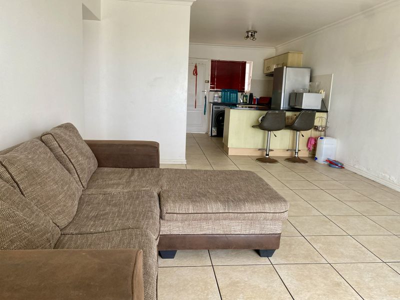 Open-plan living area featuring tiled flooring and a functional kitchen with a breakfast bar, offering a versatile space for living and dining.