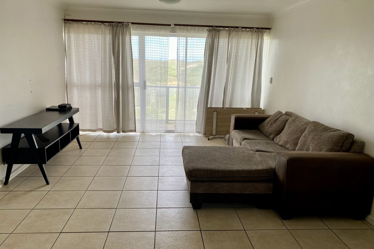A living room featuring neutral tiled flooring and a large sliding glass door that provides natural light and access to the balcony.