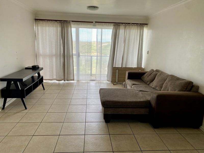 A living room featuring neutral tiled flooring and a large sliding glass door that provides natural light and access to the balcony.