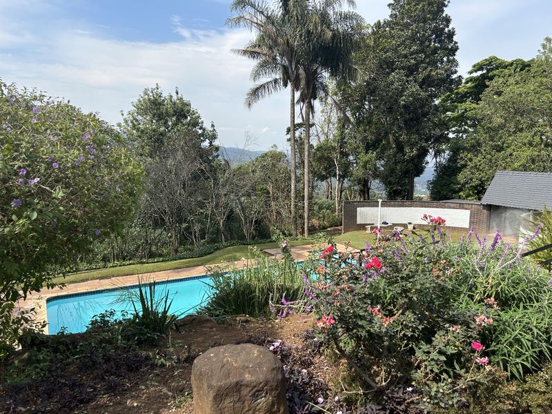 A scenic outdoor pool area featuring a swimming pool, landscaped garden, and a brick retaining wall with elevated views of the surrounding landscape.