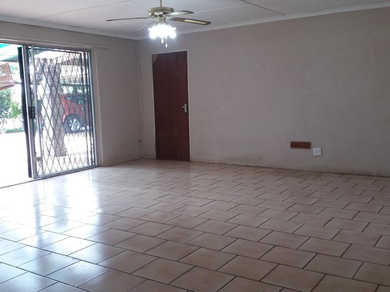 An empty living room featuring tiled flooring, a ceiling fan, and a sliding glass door with a security gate leading to the exterior.
