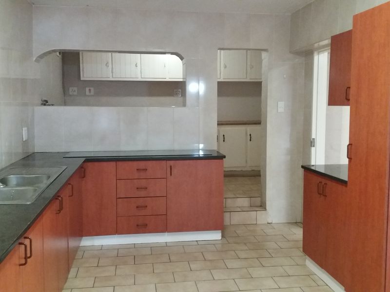 A functional kitchen featuring laminate cabinetry, granite countertops, a double bowl sink, and tiled finishes, with a convenient pass-through window to the adjacent space.