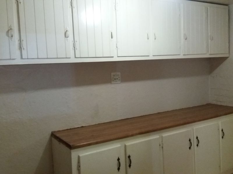 A functional scullery or utility area featuring ample upper and lower cabinetry with a wooden countertop and wall-mounted electrical outlets.