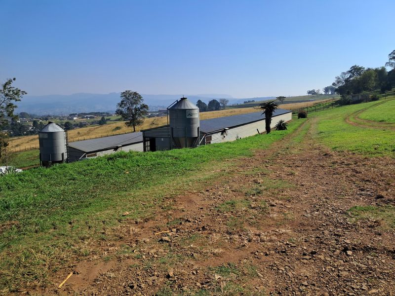View of agricultural outbuildings and metal silos on a small holding, set against a rural landscape with a dirt access track.