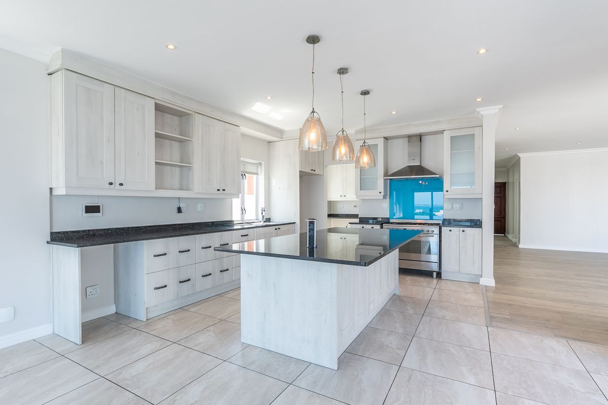 Modern kitchen featuring light wood cabinetry, a central island with granite countertops, built-in appliances, and sleek tiled flooring in an open-plan layout.
