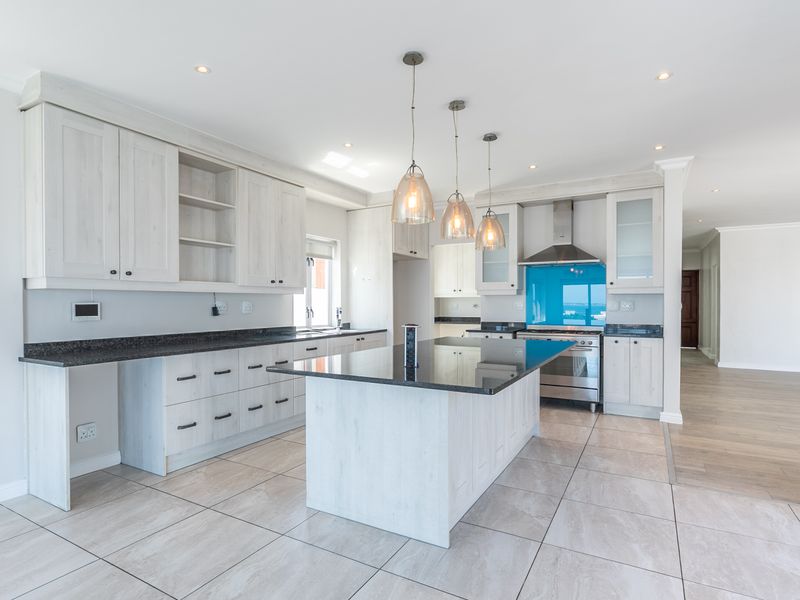 Modern kitchen featuring light wood cabinetry, a central island with granite countertops, built-in appliances, and sleek tiled flooring in an open-plan layout.
