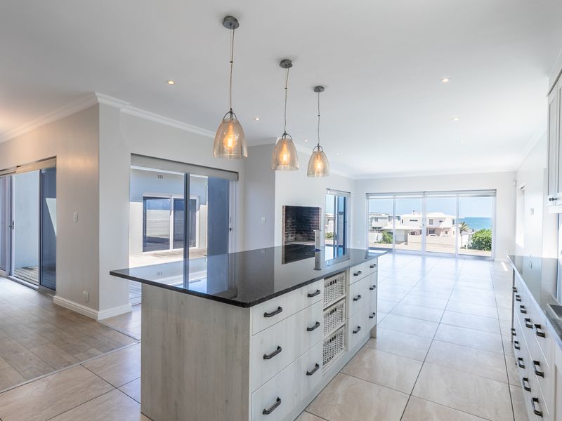Spacious open-plan living and kitchen area featuring a large island with granite countertops, modern pendant lighting, and expansive sliding doors leading to the outdoors.