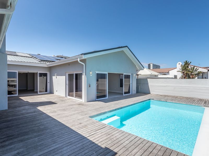 Outdoor entertainment area featuring a swimming pool, extensive timber decking, and direct access to the home through large sliding glass doors.