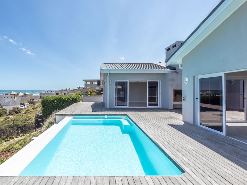 Spacious outdoor entertainment area featuring a swimming pool, extensive timber decking, and seamless indoor-outdoor flow through large sliding glass doors with coastal views.