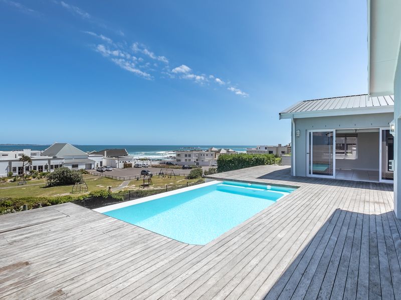 Outdoor pool area featuring timber decking and sliding glass doors, offering expansive coastal and neighbourhood views.