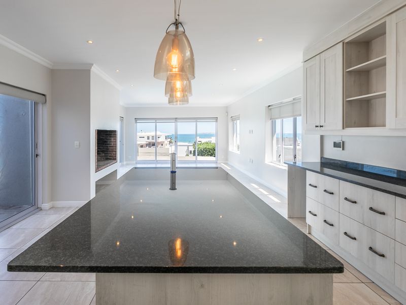 Spacious open-plan kitchen and living area featuring a large island with granite countertops, modern cabinetry, and seamless access to an outdoor patio with ocean views.