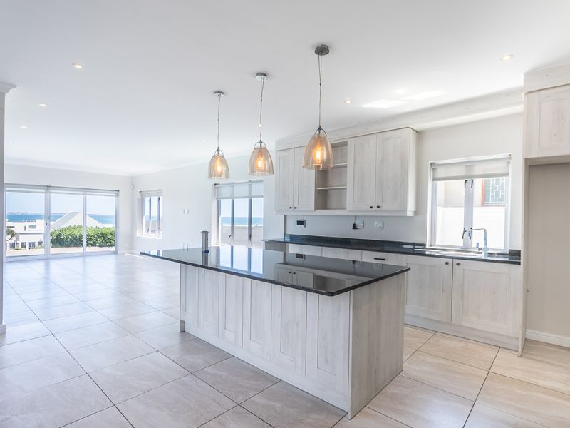 Spacious open-plan kitchen and living area featuring a central island, granite countertops, light wood cabinetry, and large sliding doors with ocean views.