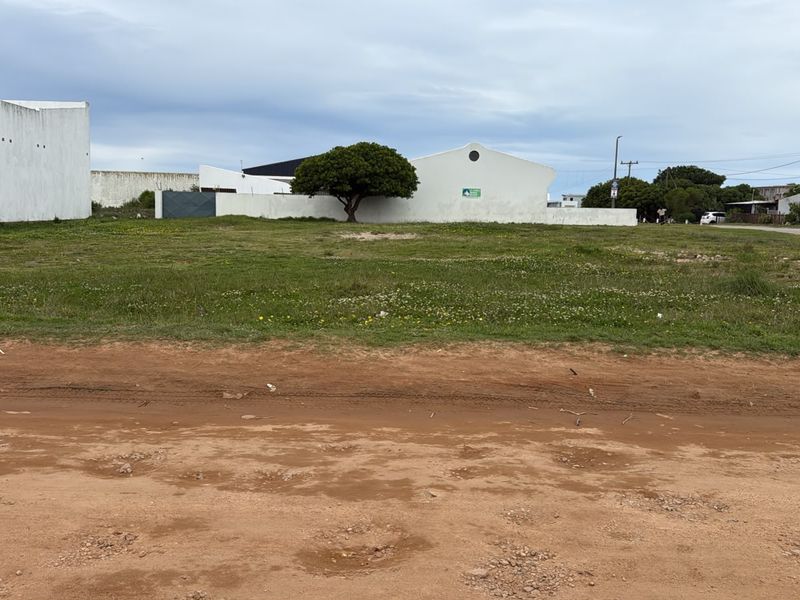 A vacant residential plot featuring level ground, boundary walls, and direct access from an unpaved road, ready for development.