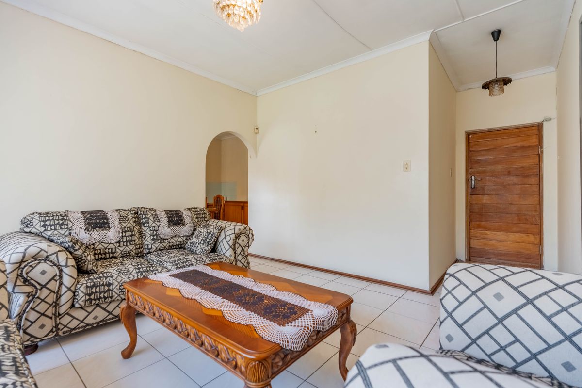 A living room featuring tiled flooring, a classic archway leading to an adjacent space, and a solid wooden door.