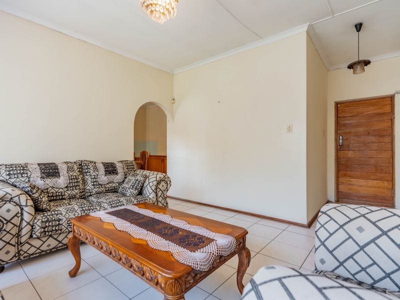 A living room featuring tiled flooring, a classic archway leading to an adjacent space, and a solid wooden door.