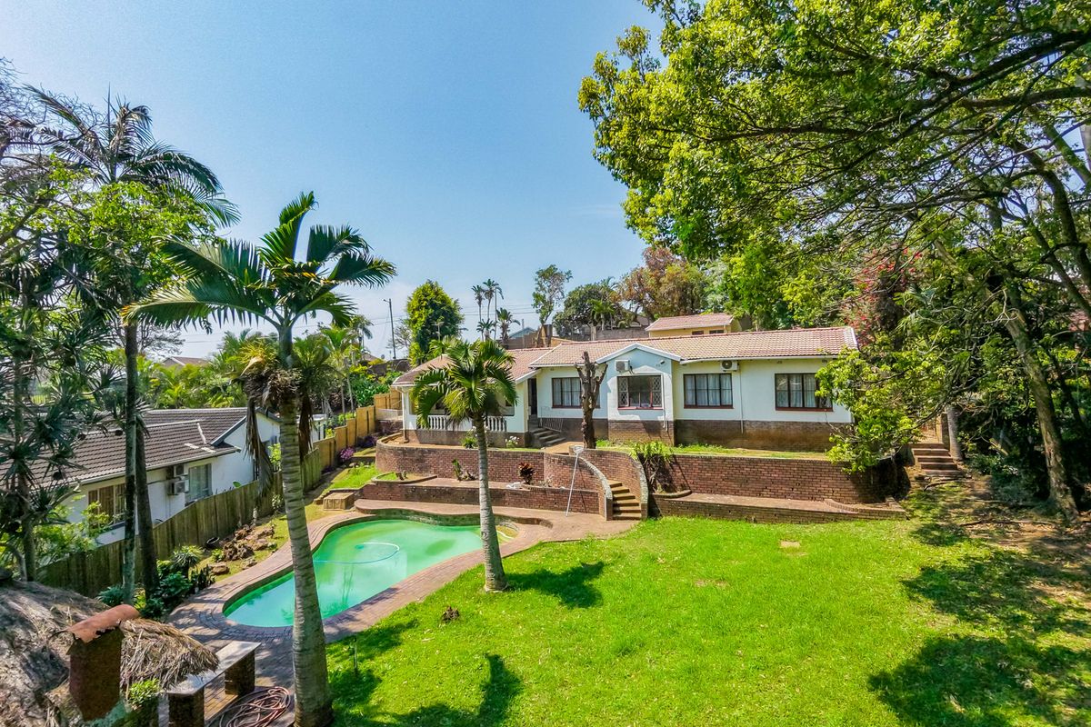 Rear view of the property featuring a swimming pool, tiered brick retaining walls, and a spacious garden area with mature trees.