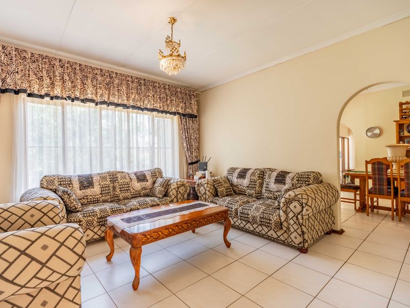A spacious living room featuring ceramic floor tiles, a decorative crystal chandelier, and an arched entryway leading to the adjacent dining area.
