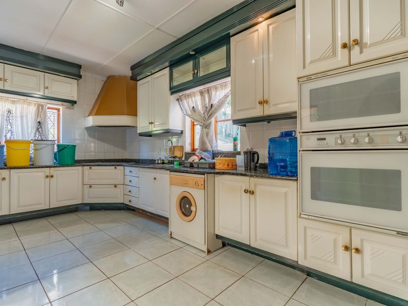 A spacious kitchen featuring traditional white cabinetry, granite countertops, a double wall oven, and tiled flooring, offering a functional layout with ample storage space.