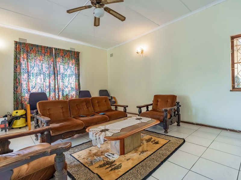 A living room featuring tiled flooring, a ceiling fan, and a window with a security gate, requiring cosmetic updates to modernize the space.