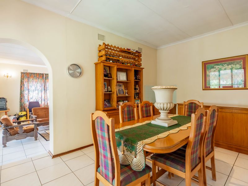 A dining room featuring tiled flooring and an arched entryway leading to an adjacent living space, with built-in cabinetry providing storage.