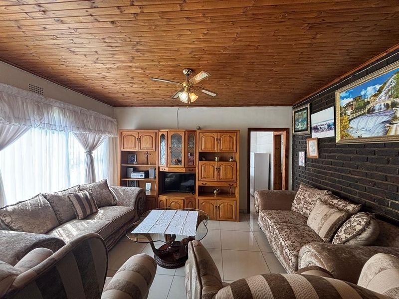 A living room featuring a warm timber ceiling, exposed brick feature wall, and tiled flooring, offering a cozy and traditional atmosphere.