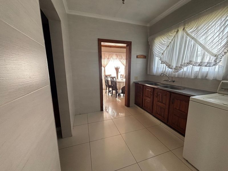 A functional scullery area featuring built-in wooden cabinetry, a double stainless steel sink, and clean tiled finishes, providing convenient additional prep and wash-up space.