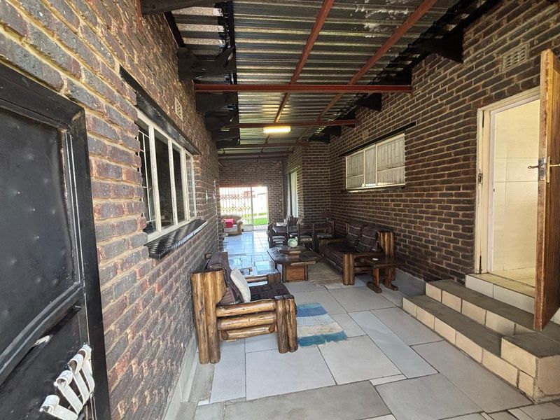 A covered outdoor patio area featuring exposed brick walls, tiled flooring, and a corrugated metal roof structure, providing a functional space for outdoor living.