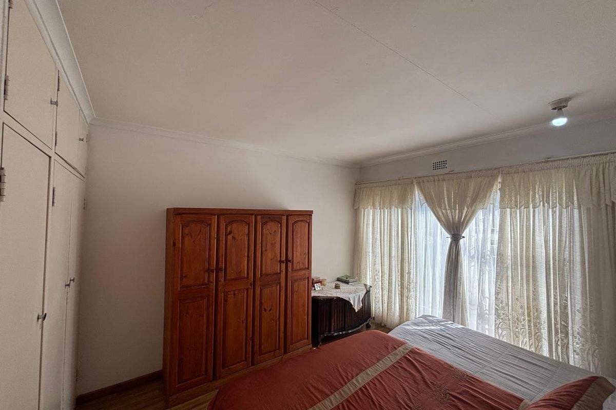 A bedroom featuring built-in cupboards, laminate flooring, and large windows with curtains, offering a functional space with potential for modern updates.