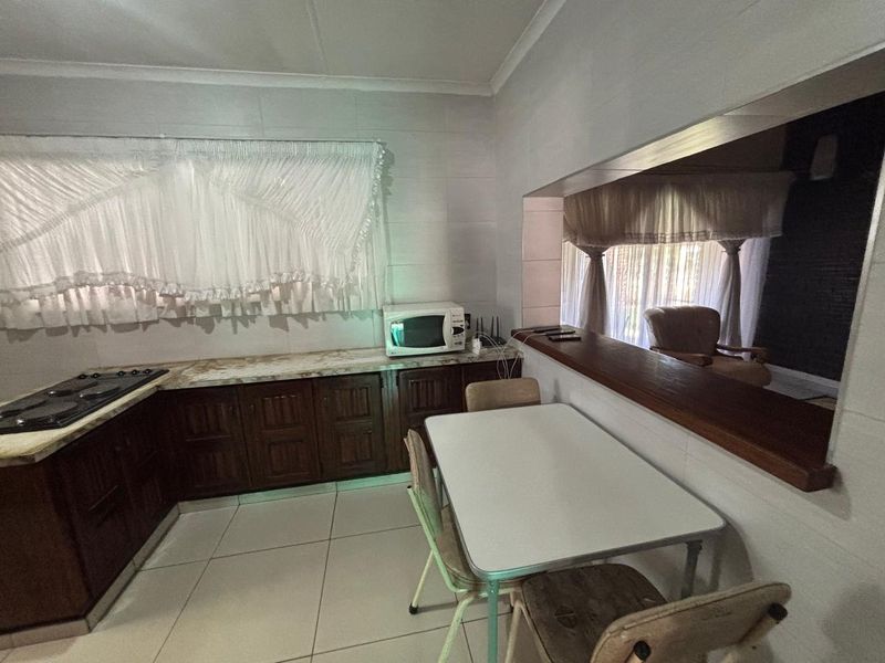 A functional kitchen featuring dark wood cabinetry, laminate countertops, a built-in hob, and a convenient pass-through window connecting to the adjacent living area.