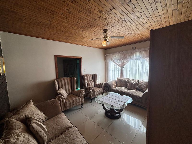 A living room featuring a timber tongue and groove ceiling, ceiling fan, and tiled flooring, offering a warm and traditional aesthetic.