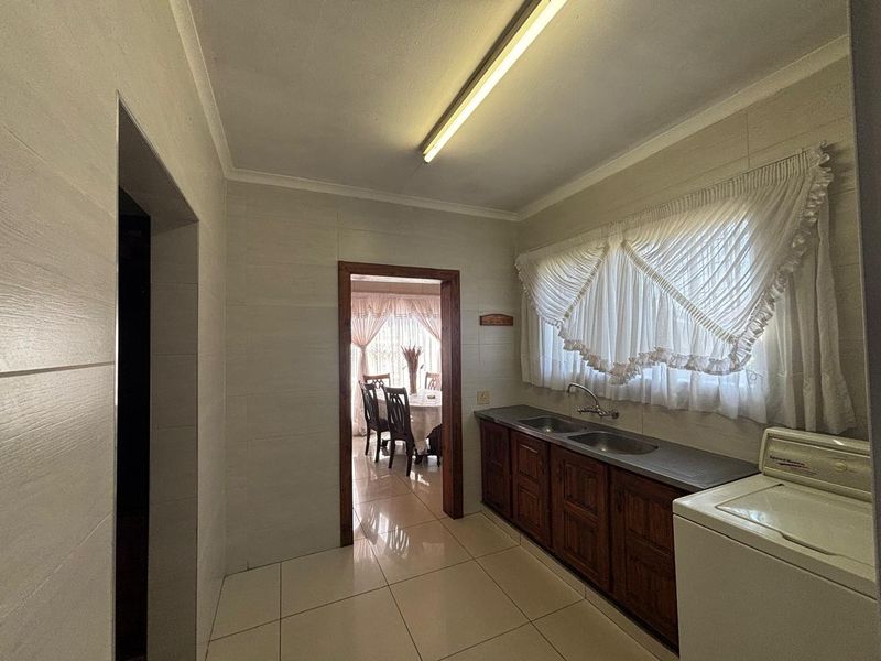 A functional scullery area featuring built-in wooden cabinetry, a double stainless steel sink, and tiled flooring, providing convenient additional workspace.