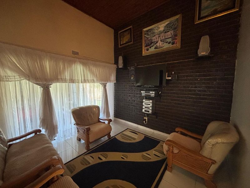 A living room featuring a dark exposed brick feature wall, tiled flooring, and a timber ceiling, offering a cozy and traditional aesthetic.