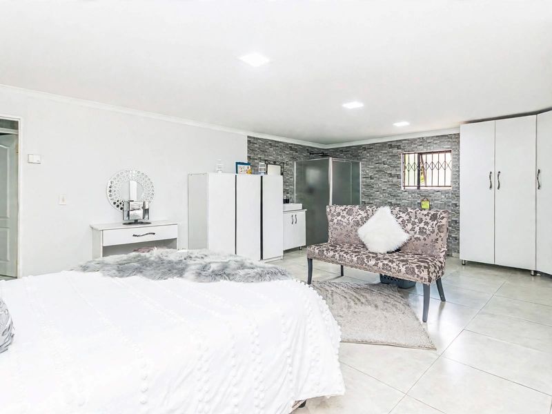 Spacious bedroom featuring tiled flooring, a stone-cladding accent wall, built-in cupboards, and an en-suite bathroom.