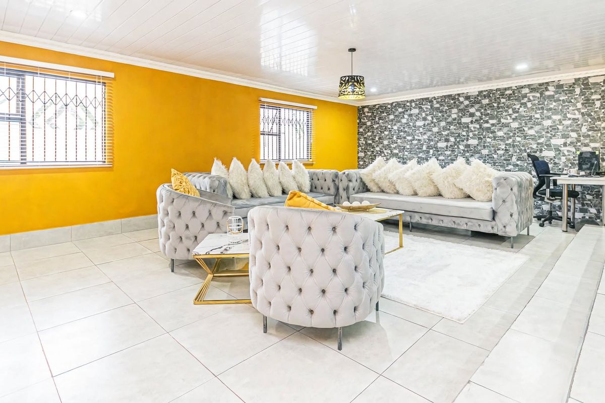 Spacious living room featuring tiled flooring, a stone-effect feature wall, and security bars on the windows.
