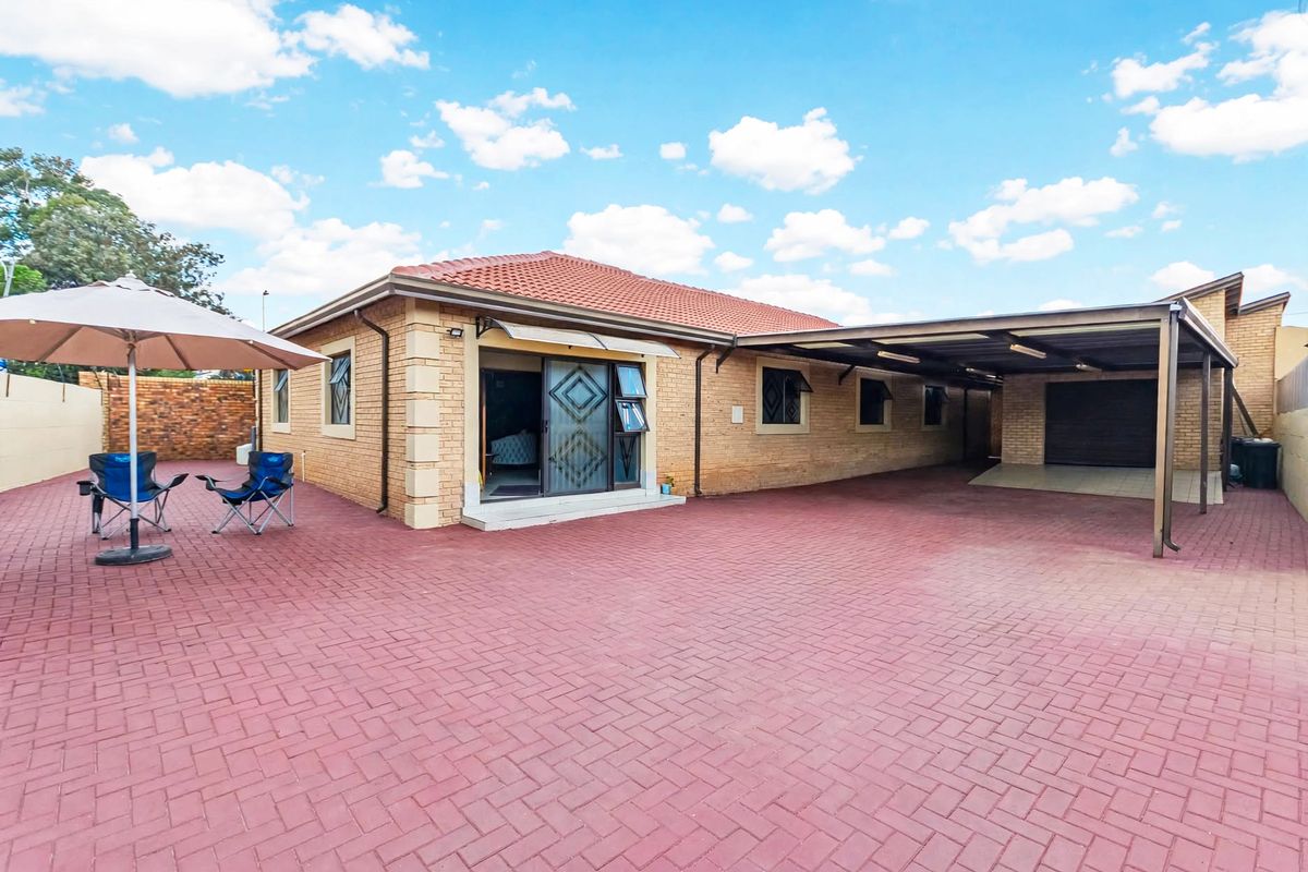 Rear view of a brick house featuring a large paved courtyard, a covered carport, and sliding door access to the interior.