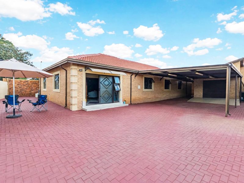 Rear view of a brick house featuring a large paved courtyard, a covered carport, and sliding door access to the interior.
