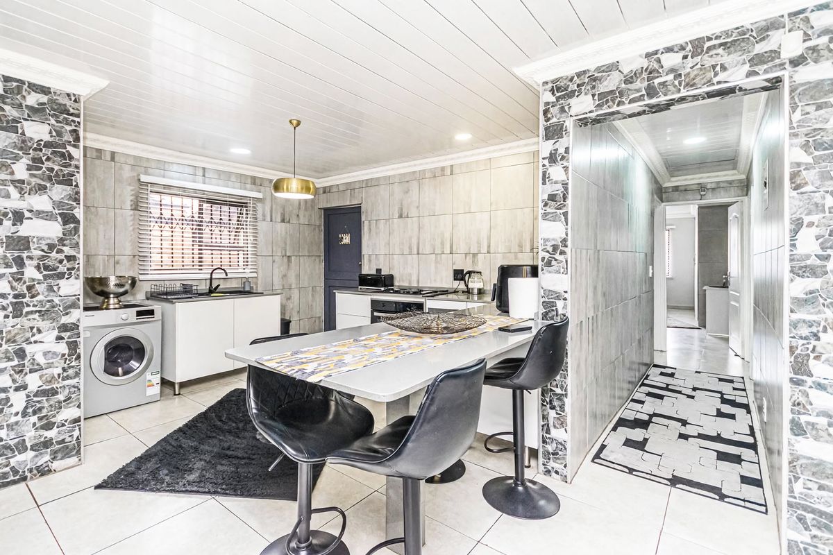 Modern kitchen featuring tiled walls, built-in cabinetry, integrated oven, hob, and a breakfast bar area with direct access to the hallway.